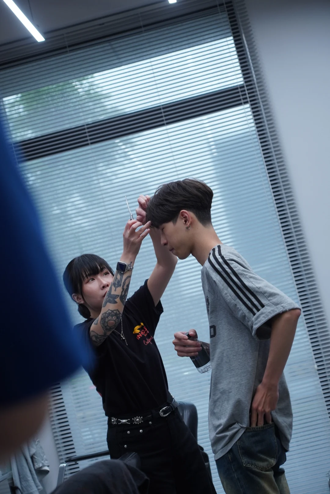 A designer arranging hair around a client's forehead beside the window
